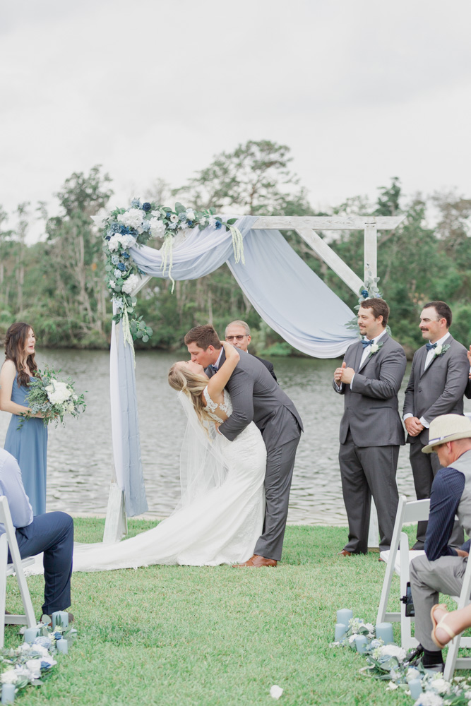 First kiss backyard lakeside wedding | dusty blue and white and grey
